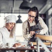 Kvinnlig kock och servitris tittar på ipad och använder kalkylator. Foto